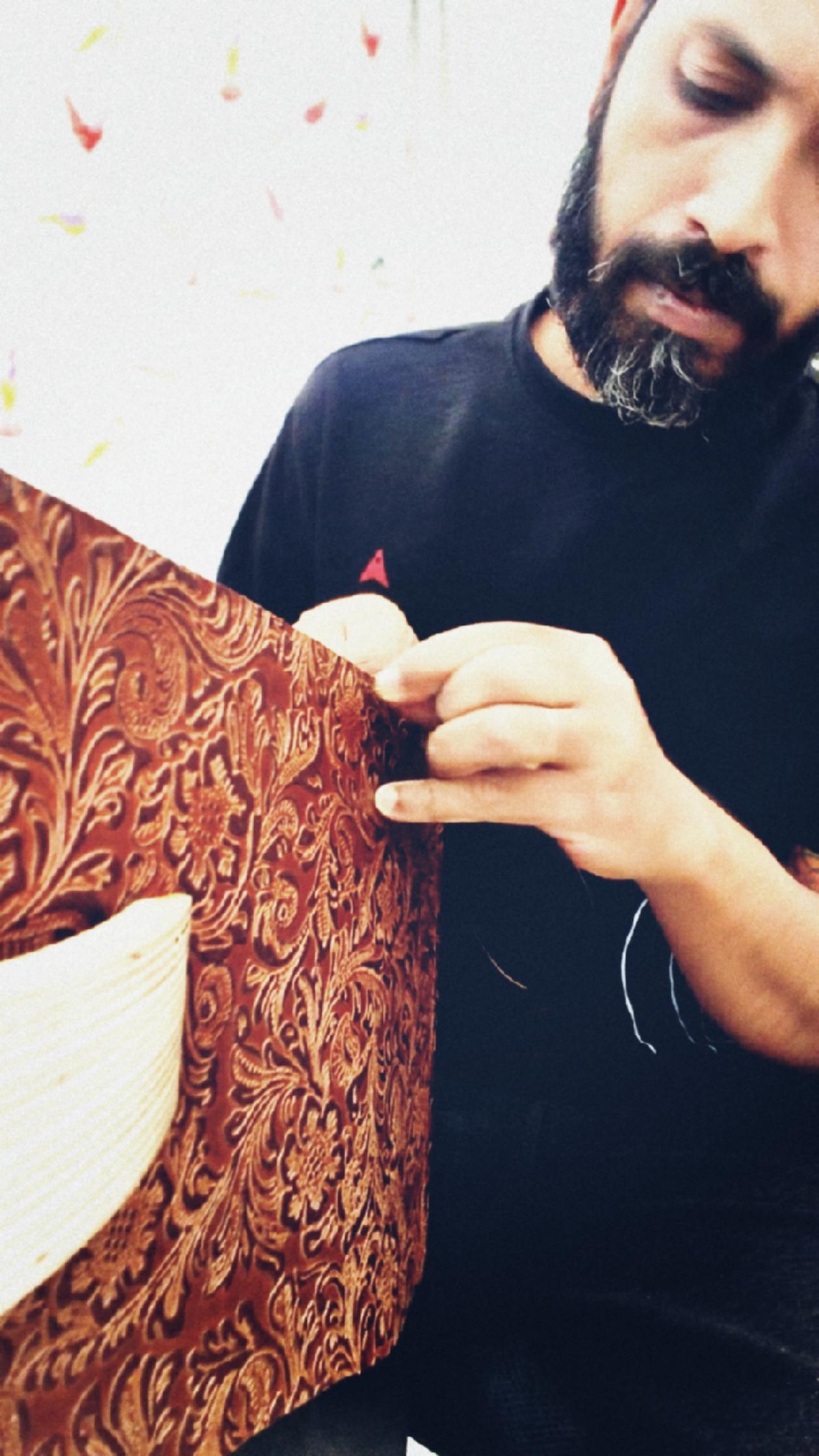 The maker hand-stitching an embossed floral leather panel at the Tassma bench