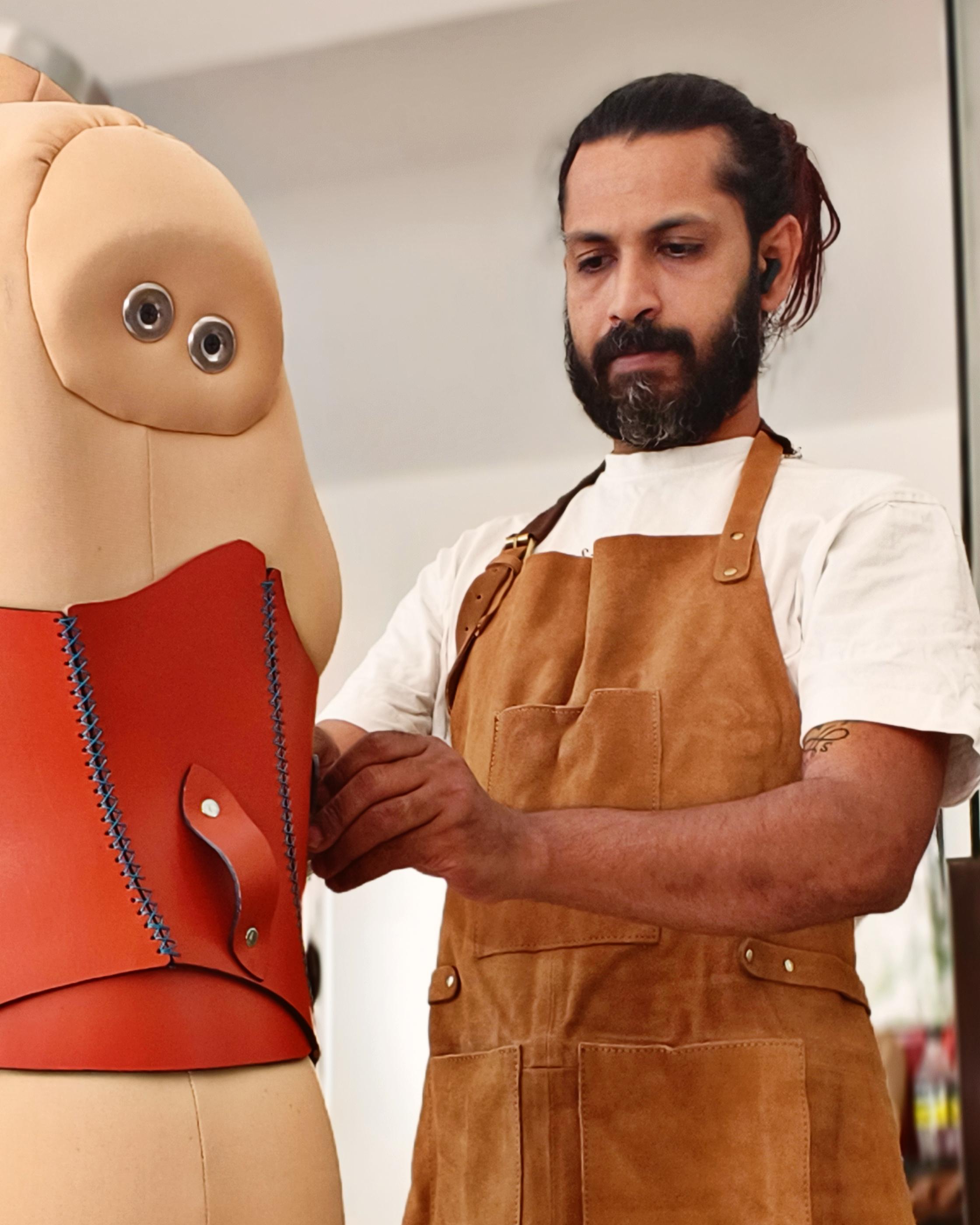 The maker of Tassma, in a work apron, fitting a hand-stitched red leather corset on a dress form in Hyderabad, India